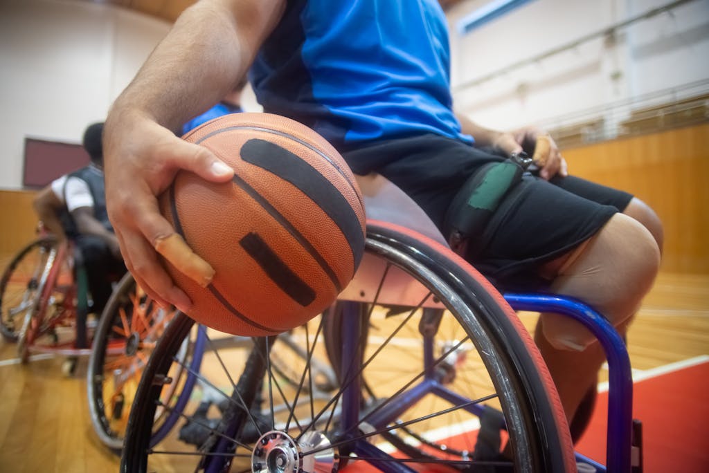 Close-Up Shot of a Person Sitting on Wheelchair while Holding a Ball
